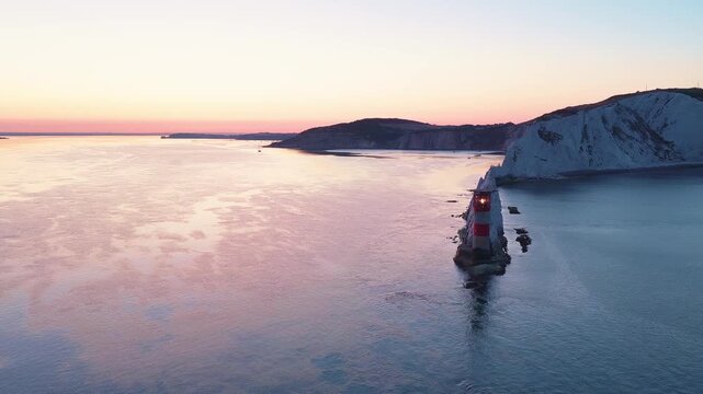 4K wide-angle drone footage panning across The Needles Lighthouse, chalk stacks and western Isle of Wight headland beneath golden sunrise skies.