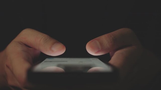 Close-up of Hand Holding and Scrolling Smartphone Screen in Dim Warm Light Room at Night.