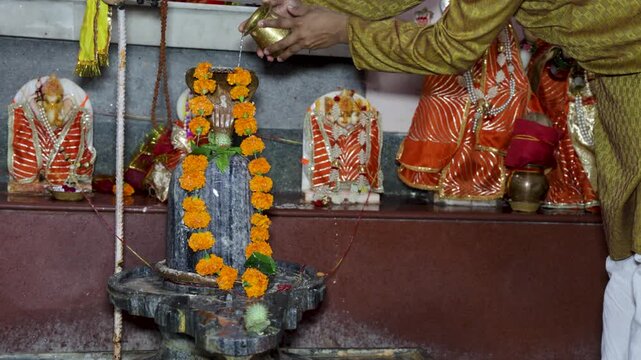 Hindu Worshipper Offering Sacred Water to Shiva Lingam During Temple Puja