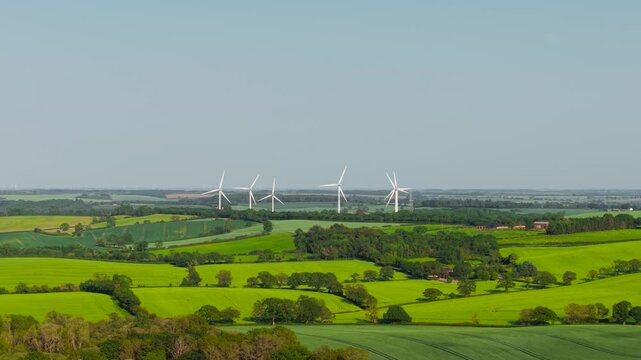 Renewable energy expanding across patchwork fields and countryside landscape. Wind turbines producing sustainable electricity for modern power infrastructure. Clean technology supporting carbon
