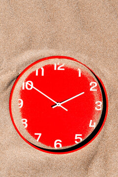 a red clock rests half hidden on the beach