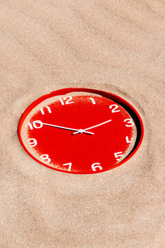 a red clock lies almost flush with beach sand