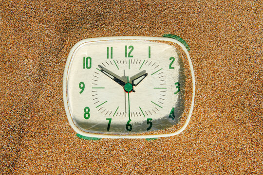 seen from above, a clock emerges from beach sand