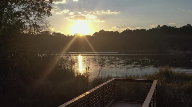 Stunning view of the sun setting over a peaceful lake, its golden rays reflecting on the water's surface as mist rises and the camera pans across the tranquil landscape with a wooden pier