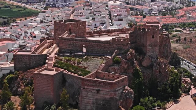 Drone footage flying over Salobre&ntilde;a castle interior &mdash; courtyard, inner walls, and turrets revealed below as the whitewashed town and palm-lined seafront stretch beyond.