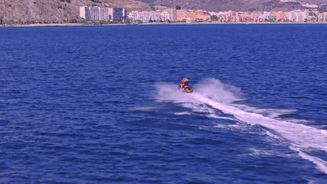 Drone footage following behind a jetski at speed &mdash; riders carving through choppy Mediterranean swells, Almu&ntilde;ecar's beach hotels and hillside visible on the horizon.