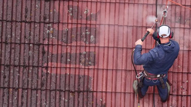 Roof cleaning with pressure washer on historic building during renovation and maintenance of traditional roof tiles. Professional roof cleaning service using pressure washer.