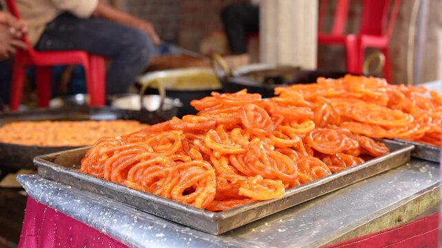 Freshly made traditional Indian sweet jalebi piled high on metal trays at an outdoor street food market stall. Traditional Indian sweet jalebi