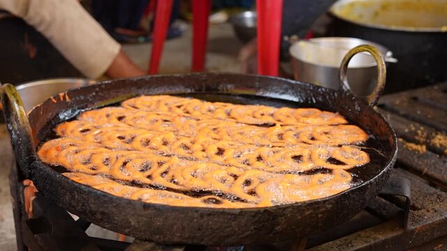 Frying traditional Indian sweet jalebi in a large pan with hot boiling oil at an outdoor street food market stall. traditional crispy jalebi dessert
