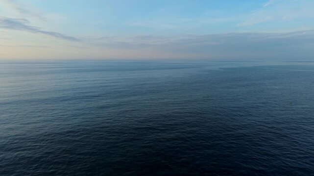 Open Atlantic Ocean with calm dark blue waters, soft pastel horizon and scattered clouds at dusk off Gloucester Massachusetts New England USA, aerial dolly right