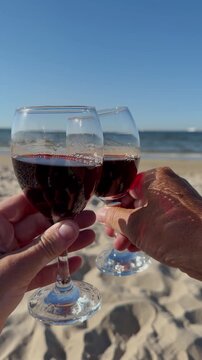 Two glasses of red wine in the hands of a man and a woman on the shore of the Baltic Sea, Poland