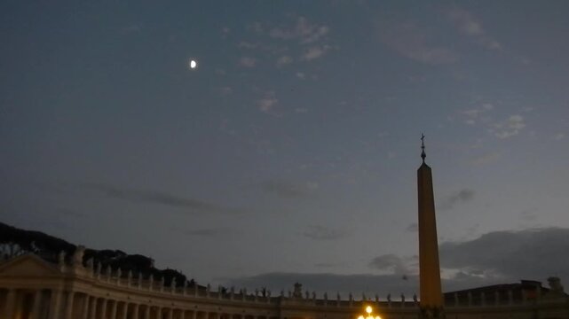 Dark night sky with moon and flying birds over Vatican Egyptian obelisk with cross in Square of St. Peter in Rome in Italy. Topics: tourist attraction, tourism, art, history, symbol, christianity