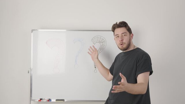 person performing hand gestures in front of a whiteboard with markers visible against a plain white wall in a neutral instructional setting, static frontal shot.