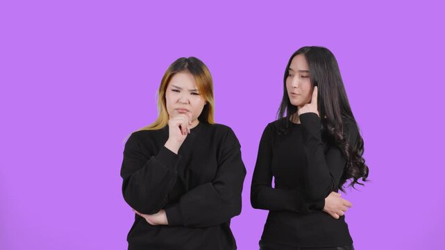 Two thoughtful women generating ideas together on purple studio background