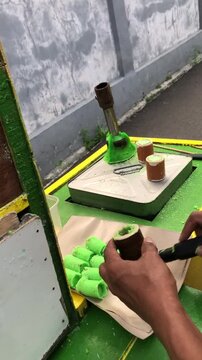 Street vendor preparing traditional green cylindrical snack called 'Kue Putu' on a small portable gas stove.