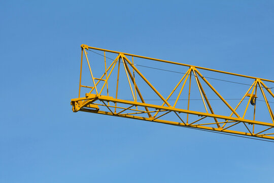 A bright yellow construction crane jib stands out clearly against a cloudless blue sky. Concept of urban growth and construction.