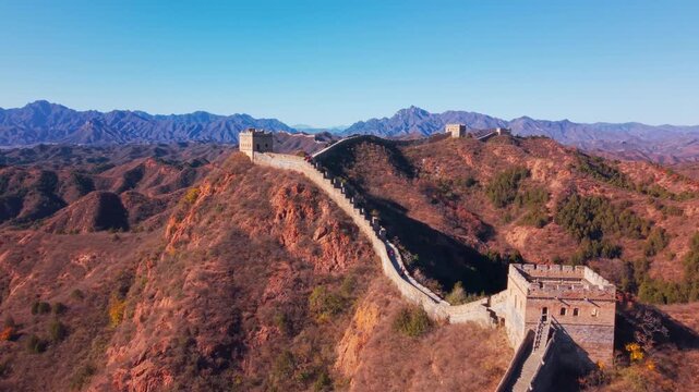 High angle view of the historic Great Wall of China winding across autumn hills with stone watchtowers under a clear blue sky