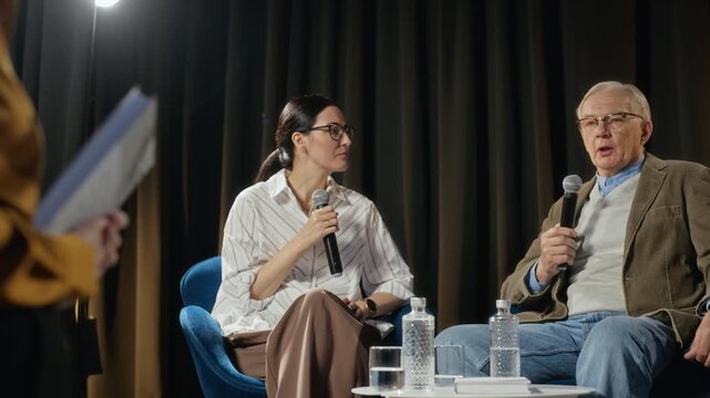 Handheld shot of Caucasian middle aged woman moderating panel discussion with woman and senior man on stage. Perfect for corporate communication, educational seminars, and public speaking promotions