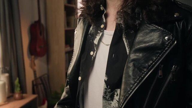 Midsection shot of unknown man adjusting black leather jacket and patterned shirt indoors. Footage for youth fashion marketing, alternative lifestyle branding, and apparel commercials