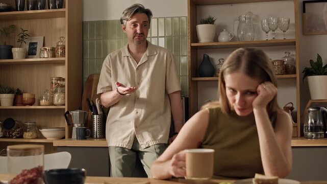 Rack focus shot of adult Caucasian woman ignoring middle aged Caucasian man during argument in kitchen. Clip ideal for relationship counseling, family therapy, or mental health awareness campaigns