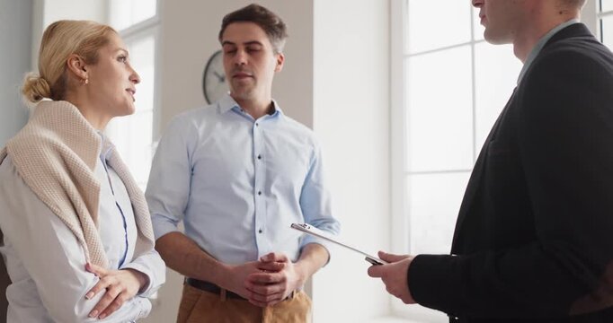 Realtor meets couple clients for property viewing. Professional agent offers consultation to buyers on apartment features, pricing and steps during a meeting. Neat realty concept for ads.