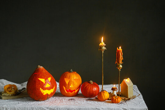 Glowing jack o lantern, carved pumpkins, spooky spiders and burning candles on dark moody background. Happy Halloween. Atmospheric Halloween preparation and decorations, space for text
