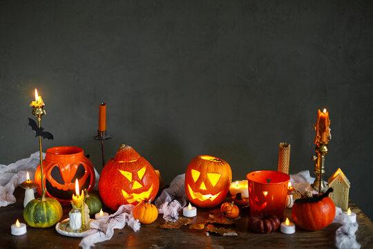 Happy Halloween. Carved halloween pumpkins with burning candles, spiders, bats on table against dark background. Atmospheric halloween decorations, holiday banner