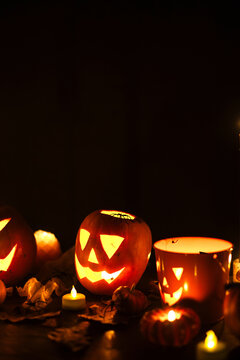 Jack o lantern glowing pumpkins, spooky spiders and burning candles on dark moody background. Happy Halloween. Spooky atmospheric halloween night, space for text. Trick or treat