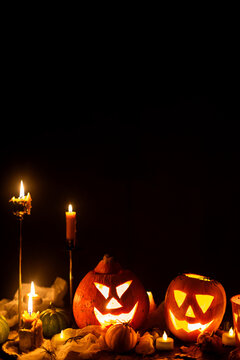 Jack o lantern glowing pumpkins, spooky spiders and burning candles on dark moody background. Happy Halloween. Spooky atmospheric halloween night, space for text. Trick or treat