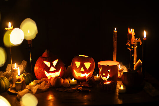 Happy Halloween. Jack o lantern glowing pumpkins, spooky spiders and burning candles on dark moody background. Spooky atmospheric halloween night, space for text. Trick or treat