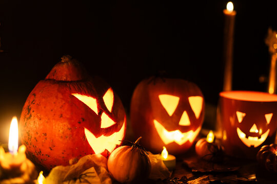 Jack o lantern glowing pumpkins, spooky spiders and burning candles on dark moody background. Happy Halloween. Spooky atmospheric halloween night, space for text. Trick or treat