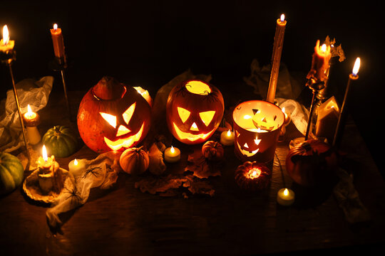 Happy Halloween. Jack o lantern glowing pumpkins, spooky spiders and burning candles on dark moody background. Spooky atmospheric halloween night, space for text. Trick or treat