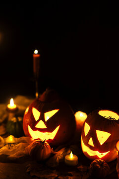 Happy Halloween. Jack o lantern glowing pumpkins, spooky spiders and burning candles on dark moody background. Spooky atmospheric halloween night, space for text. Trick or treat