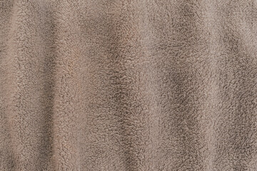Horizontal close up shot of a warm beige fleece fabric texture with soft vertical folds demonstrating a thick cozy plush material surface for winter clothing © moryachka
