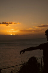 Obraz premium Person Silhouette Reaching Toward the Sunset Over the Atlantic Ocean