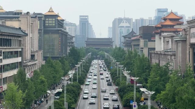 Busy city street with heavy traffic in Xian. Cars driving on road surrounded by trees and traditional China architecture. Modern urban infrastructure and commuting in a large Chinese metropolis.