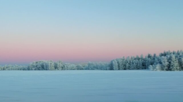 Train window view from Kajaani to Helsinki showing snow covered forest and sunset horizon at evening - Finland