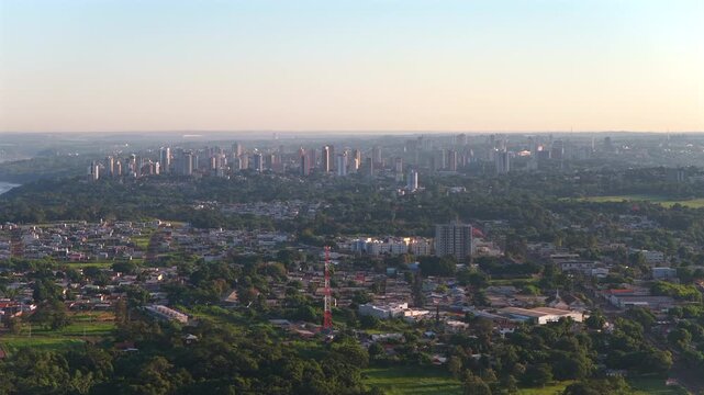 Skyline of Foz do Igua&ccedil;u rises above a vast urban landscape in Paran&aacute;, Brazil, surrounded by subtropical vegetation and warm sunrise light, slow push in aerial cityscape shot.