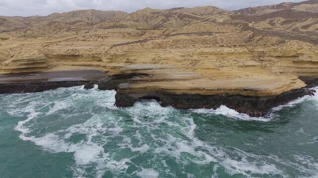An expansive aerial sequence capturing the striking patterns and deep textures of sandstone coastal bluffs meeting the Pacific Ocean near El Rosario.