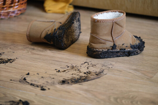 dirty boots on a messy indoor wooden floor close-up with brown and black leather, fabric, and wool materials in a home maintenance setting, ready for cleaning supplies.