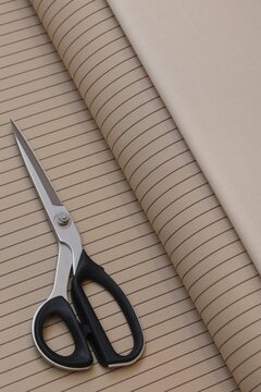 A professional tailor uses sharp shears to cut premium beige pinstripe suiting fabric, creating bespoke luxury apparel in a high-end design atelier.