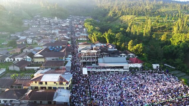 Aerial drone footage of thousands of Muslims performing the Eid al-Adha prayer in an open field in Garung, Central Java, Indonesia. Captured from above, the scene showcases a large congregation gather