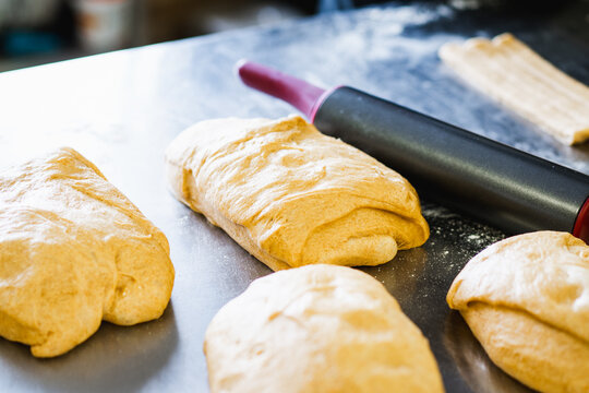 Professional baker folding and shaping sourdough dough on a floured stainless steel work surface in an artisan bakery.