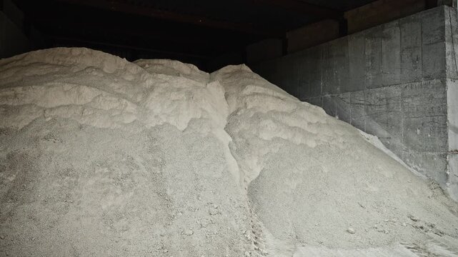 Industrial aggregate storage inside reinforced concrete bunkers with pale sand mounds, tire tracks, partition walls, rough surfaces and wide daylight industrial yard view
