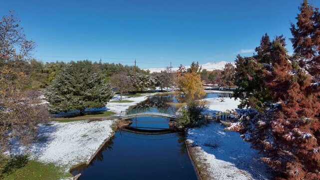 Ann Morrison Park Aerial Drone Shot Featuring Snowy Landscape River Bridge and Fall Foliage Under Clear Blue Sky in 4k Resolution Showing Beautiful Seasonal Transition Park Scenery