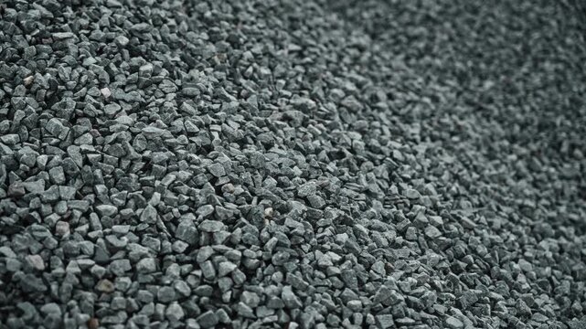 Crushed gray stone aggregate pile on diagonal slope under diffuse daylight, showing rough mineral fragments used for construction and concrete production in industrial supply context