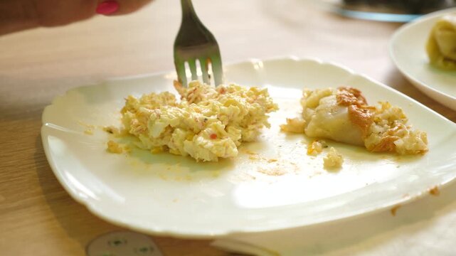 Close up of a plate as a person eats a cabbage roll and crab salad with a fork during a homemade meal.