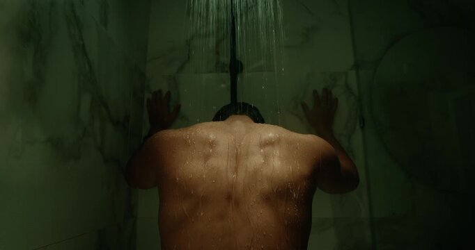 Man stand under hot water stream shower in bathroom. Depressed alone guy cry feel grief. Sad young person, gloomy atmosphere, loneliness, solitude. Melancholy mood, introspection, inner struggle.