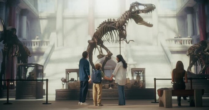 Natural History Museum Family Day Out: Mother, Father and Young Son Watch a Towering Dinosaur Skeleton Together, Learning About Prehistoric Fossils and Having Fun While Exploring the Exhibit Hall.