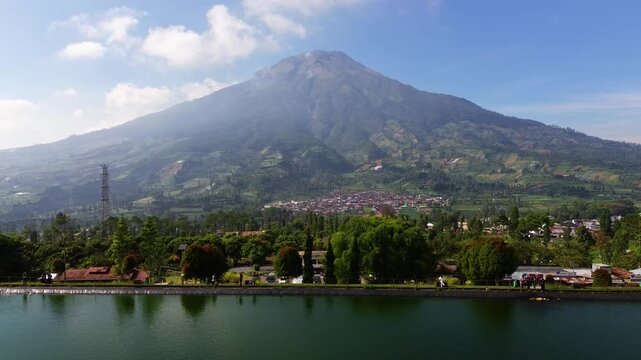 Aerial drone footage of Embung Kledung, a scenic artificial reservoir in Temanggung, Central Java, Indonesia, surrounded by the majestic Mount Sindoro and Mount Sumbing.